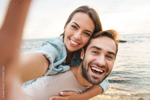 Image of man giving piggyback ride woman and taking selfie photo
