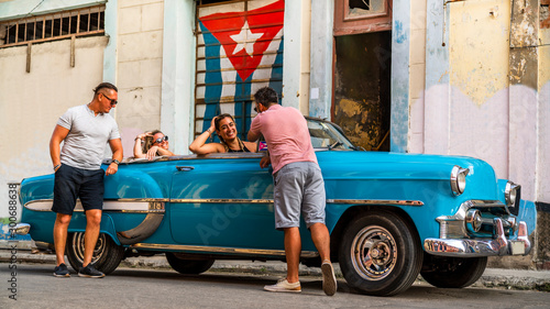 Group of multicultural friends having fun in Havana - Cuba, sightseeing the city in a trendy classic 1950 vintage car. Relaxed atmosphere of two couples spending vacation in the Caribbean country. photo