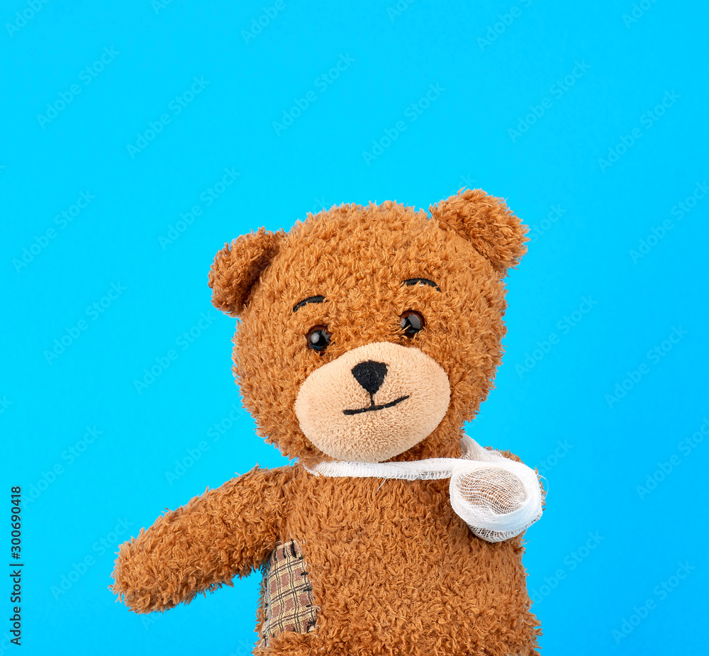 brown teddy bear with a bandaged paw sitting on a blue background brown teddy bear with a bandaged paw sitting on a blue background