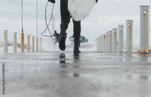 Surfing as a lifestyle. Surfers putting on wetsuits go along the city pier to the sea. Concept: winter surfing, urban surfing, lifestyle. Back view. photo