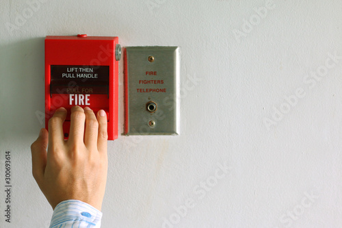 Hand of woman pulling fire alarm switch on the white wall as background for emergency case at the office