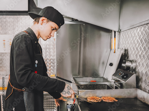 Burger making Food concept Young cook in black uniform is roasting beef for hamburgers on cafes kitchen