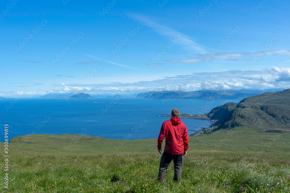 Man in red jacket looking towardsthe sea and the islands in the background. Travel, summer, weather, sun, blue sky, holiday concept.