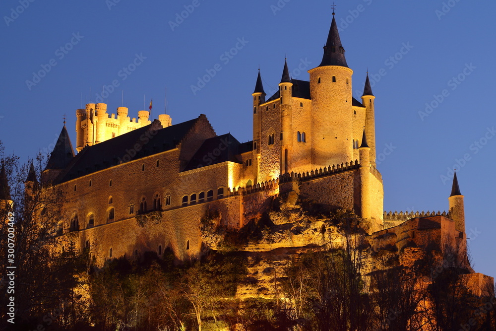 Panorámica nocturna de un castillo de fantasía situado sobre unas rocas e iluminado con focos