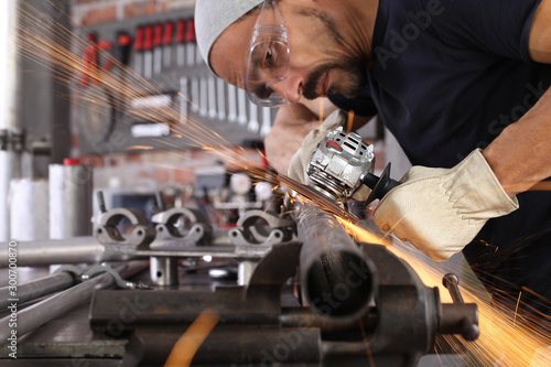 man work in home workshop garage with angle grinder, goggles and construction gloves, sanding metal makes sparks closeup, diy and craft concept