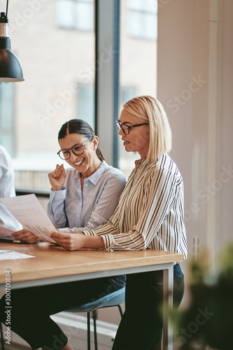 Smiling businesswomen reading paperwork together in an office bo photo