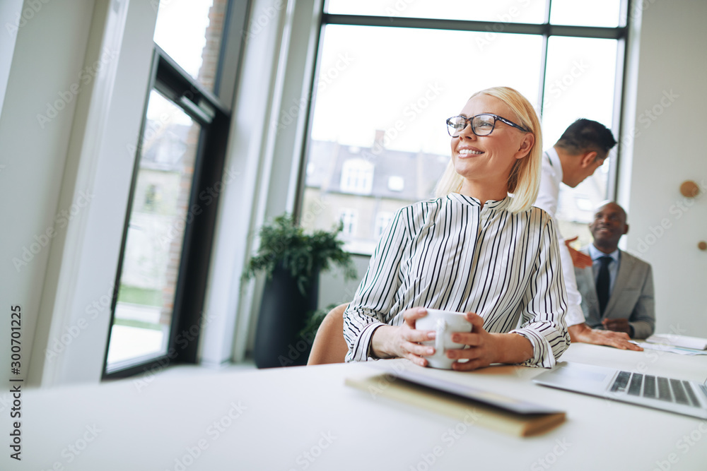 Smiling businesswoman enjoying a coffee during her office break - obrazy, fototapety, plakaty 