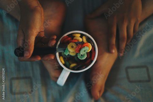 Young child having breakfast and eating colorful cereals in bed.