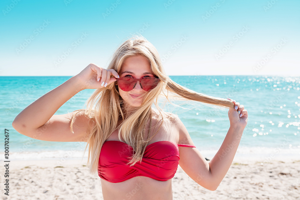 Portrait of a blonde in pink glasses at the sea. A woman walks along the beach and enjoys. Portrait of a blonde in pink glasses at the sea. A woman walks along the beach and enjoys.