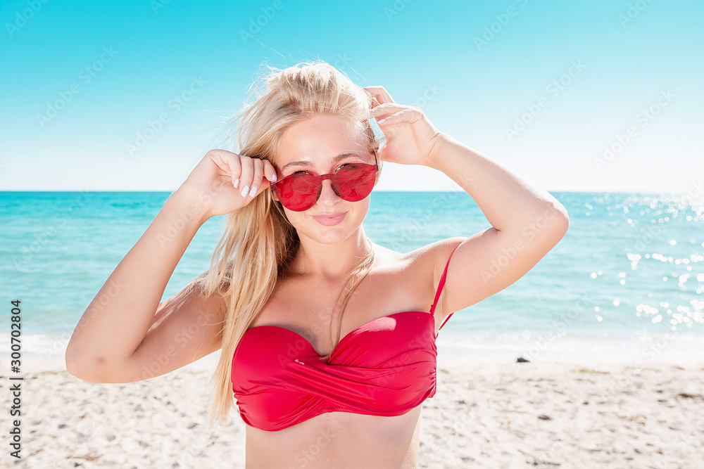 Portrait of a blonde in pink glasses at the sea. A woman walks along the beach and enjoys. Portrait of a blonde in pink glasses at the sea. A woman walks along the beach and enjoys.