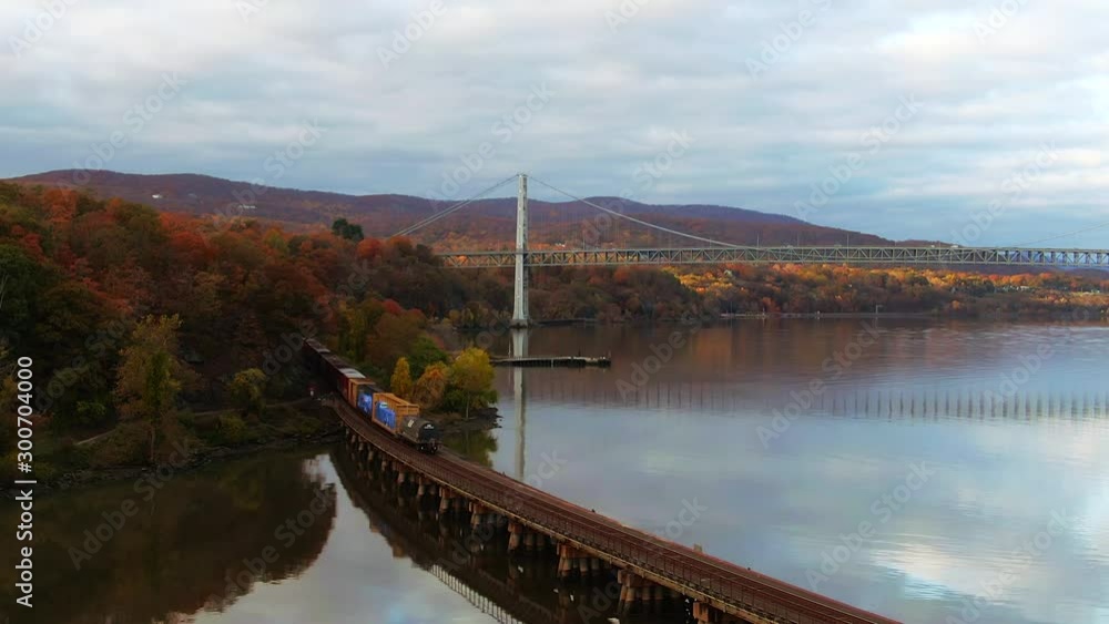 Low cinematic aerial of train moving on Hudson River with Bear Mountain Bridge fall foliage reflecting on water Low cinematic aerial of train moving on Hudson River with Bear Mountain Bridge fall foliage reflecting on water