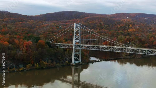 Cinematic aerial view of Bear Mountain Bridge traffic on Hudson River Valley with colorful fall foliage reflection on water photo