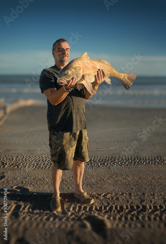 Fisherman holds a huge fish in the background of the sea. Black drum (Pogonias cromis) photo