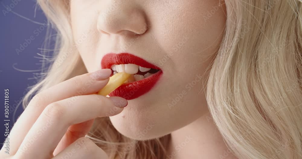 Blonde girl with red lipstick temptingly biting unhealthy french fries - diet, fast food concept close up shot 4k footage Blonde girl with red lipstick temptingly biting unhealthy french fries - diet, fast food concept close up shot 4k footage