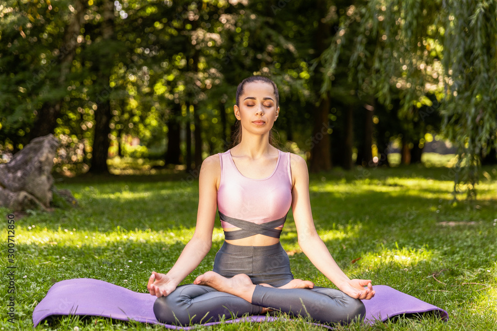 Slim girl meditating sitting in a lotus pose with closed eyes on the lawn in a park Slim girl meditating sitting in a lotus pose with closed eyes on the lawn in a park