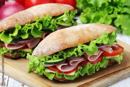 Two sandwiches with fresh vegetables, ham and cheese in ciabatta bread 