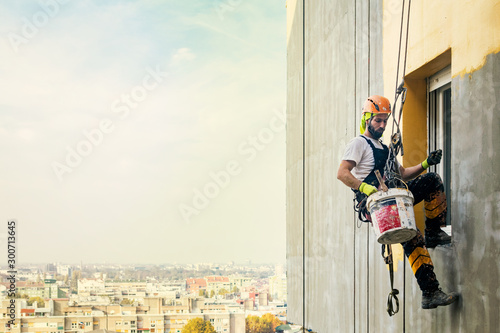 Industrial rope access worker hanging from the building while painting the exterior facade wall. Industrial alpinism concept image. Top view