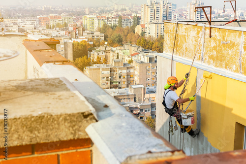 Industrial rope access worker hanging from the building while painting the exterior facade wall. Industrial alpinism concept image. Top view photo