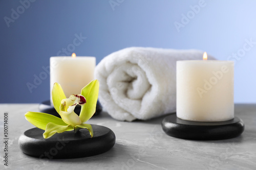 Spa stones with exotic flower and burning candles on grey table  space for text
