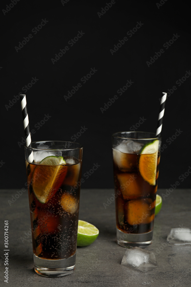 Refreshing soda drinks with straws on grey table against black background, space for text Refreshing soda drinks with straws on grey table against black background, space for text