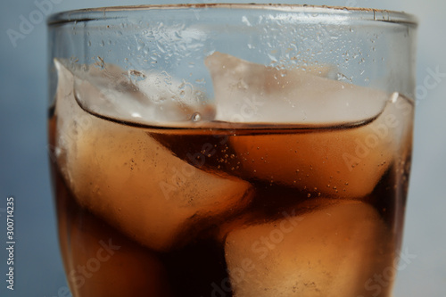 Glass of refreshing soda drink with ice cubes on blue background, closeup