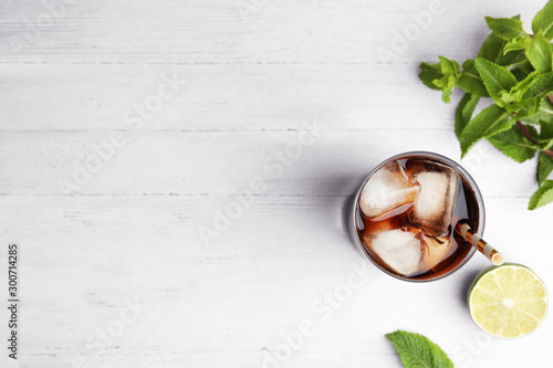 Glass of refreshing soda drink with ice cubes, mint and lime on white wooden table, flat lay. Space for text