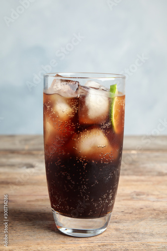 Glass of refreshing soda drink with ice cubes and lime on wooden table against blue background