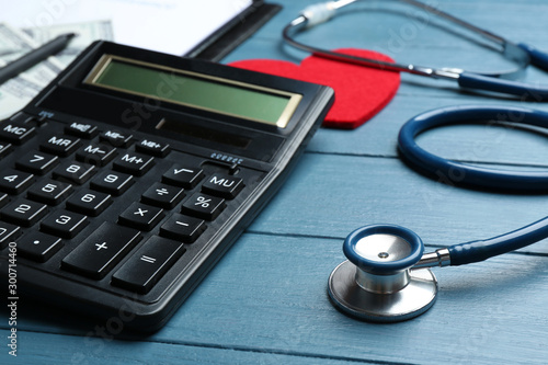 Calculator and stethoscope on blue wooden surface. Health insurance concept