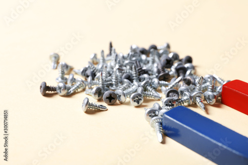 Magnet attracting screws on beige background, closeup