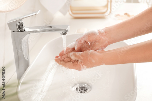 Young woman washing hands with soap over sink in bathroom, closeup