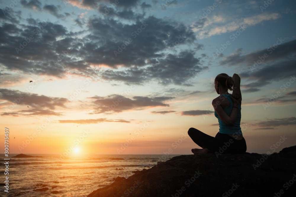 Young woman practicing yoga on the ocean coast during a sunset.