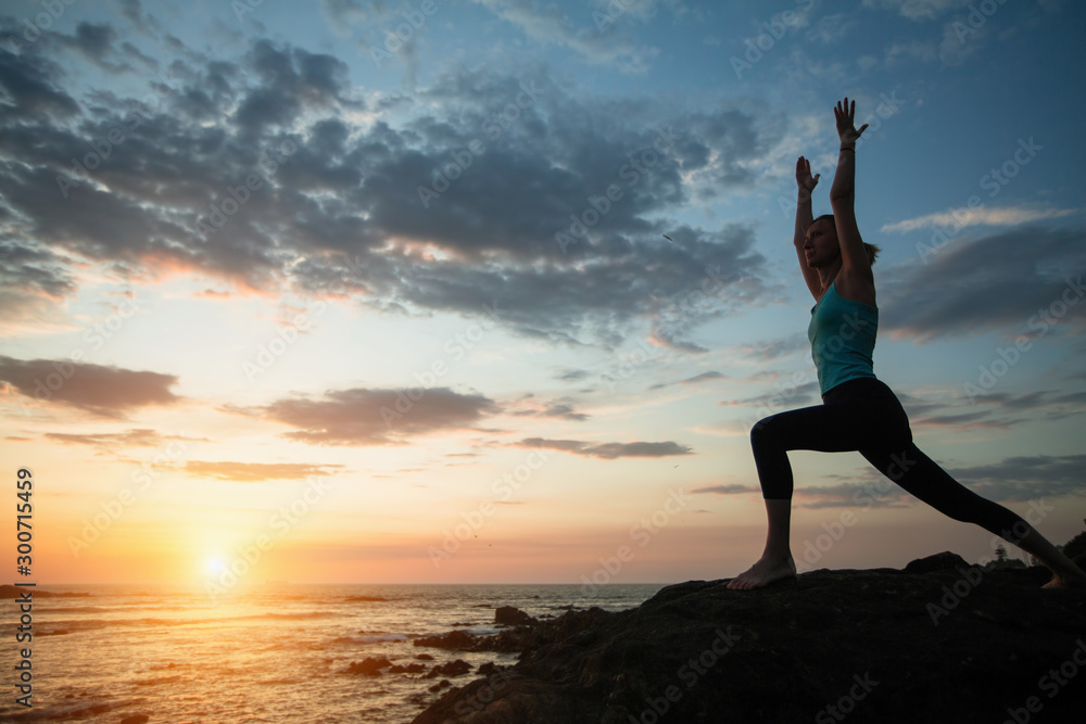 Fitness woman practicing yoga on the ocean coast during a sunset.