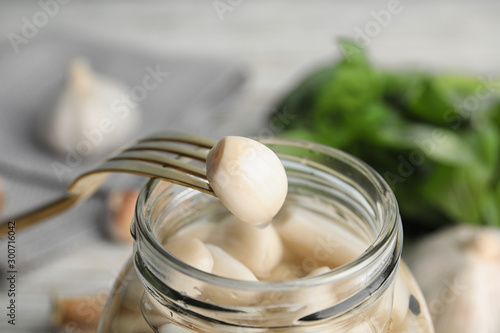 Fork with clove of pickled garlic over jar, closeup