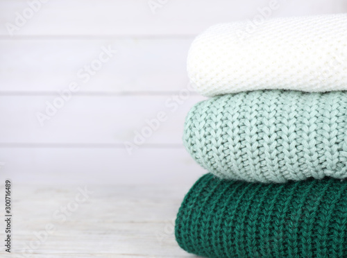 Stack of soft knitted sweaters on white wooden table. Space for text