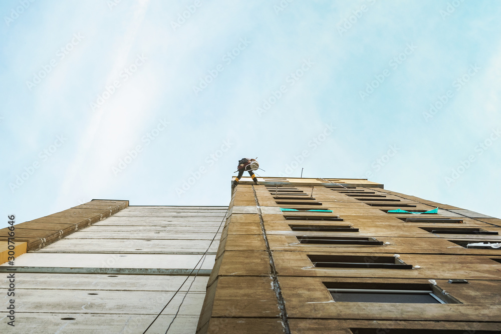 Obraz premium Industrial rope access worker hanging from the building while painting the exterior facade wall. Industrial alpinism concept image. Top view