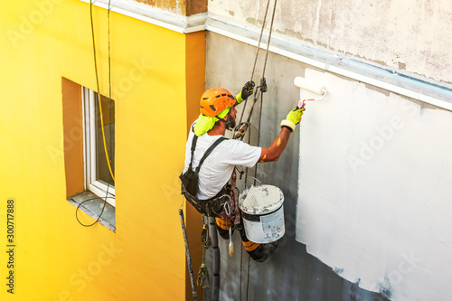 Industrial rope access worker hanging from the building while painting the exterior facade wall. Industrial alpinism concept image. Top view