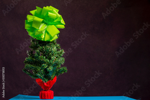 There is Christmas tree with big light green bow cone on the blue table and dark background. Merry Christmas. Happy New Year 2020. 