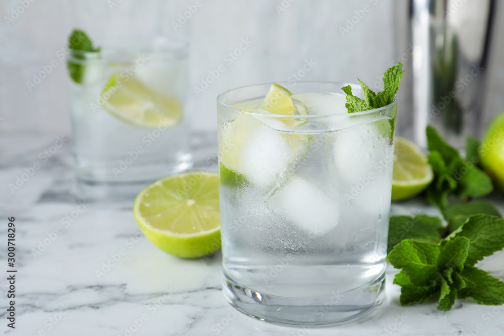 Glass of cocktail with vodka, ice and lime on white marble table Glass of cocktail with vodka, ice and lime on white marble table