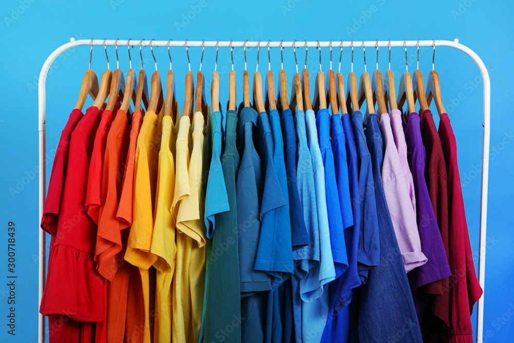 Rack with bright clothes on blue background. Rainbow colors