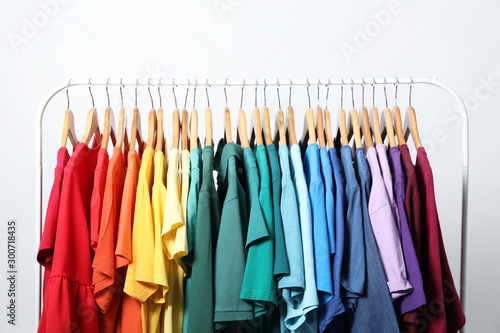 Rack with bright clothes on light background. Rainbow colors