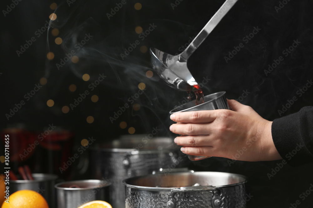 Woman pouring hot mulled wine into mug against blurred background, closeup - obrazy, fototapety, plakaty 