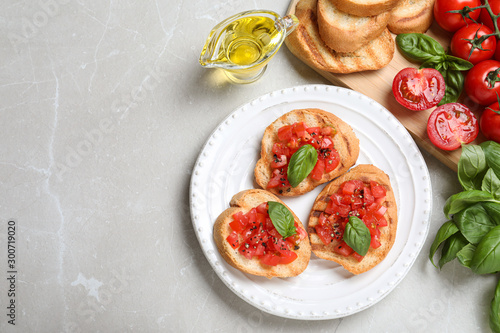 Flat lay composition of tasty bruschettas with tomatoes on light grey marble table, space for text