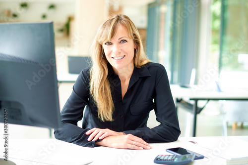 Portrai tof middle aged businesswoman sitting at office desk while looking at camera and smiling photo