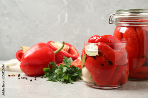 Glass jars with pickled peppers on grey table