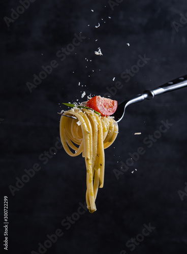 Fototapeta Naklejka Na Ścianę i Meble -  tagliatelle with tomato and pesto on fork. Italian food. Dark background