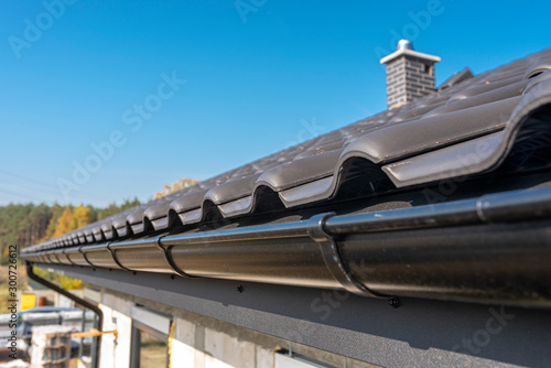 Obraz na płótnie A metal, black gutter on a roof covered with ceramic tiles