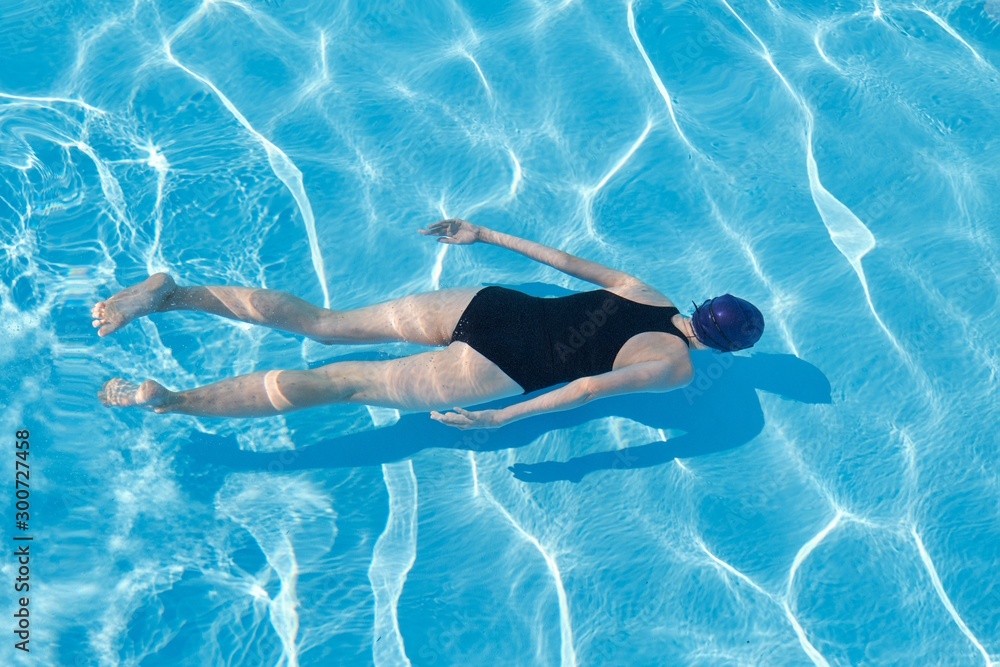 Young woman in cap sports swimsuit swimming underwater in blue outdoor pool