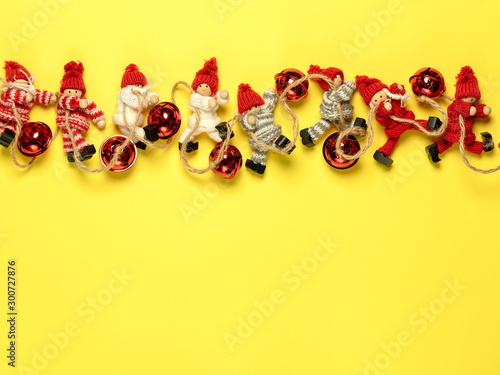 Christmas garland of colorful knitted toys in the form of men and red balls laid out in a line on a bright yellow background. The concept of Christmas and the New year. The place on the map, top view