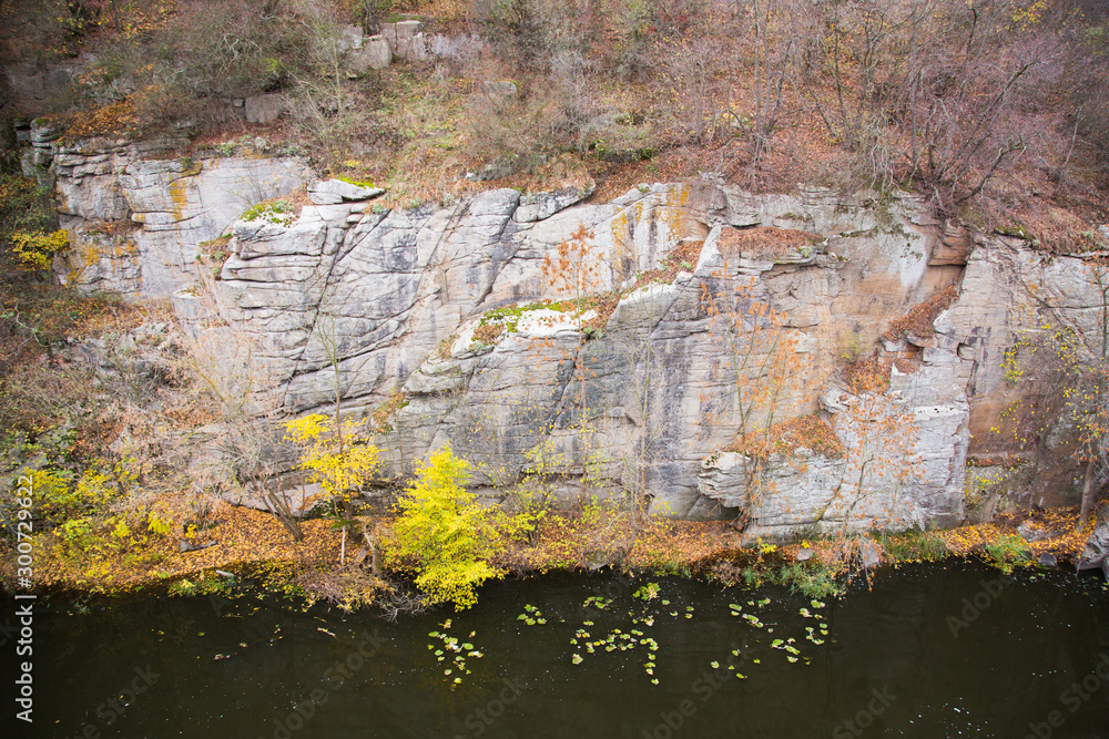View of the river and the canyon cliffs. The river flows at the foot of the cliffs. Leaves are floating on the river. Autumn landscape.