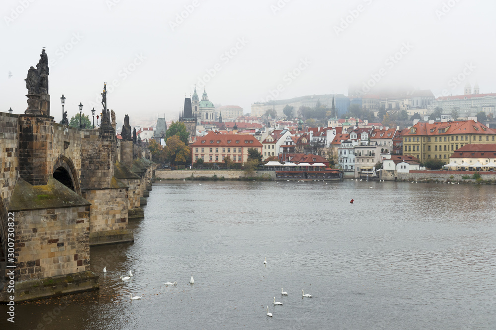 Lesser town of Prague surrounded with mists. Prague Castle complex hidden in the clouds. View of Lesser Quarter taken from opposite riverbank of Vltava nearby Charles Bridge. Fall or autumn morning.